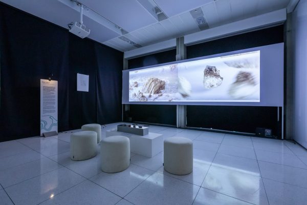 A white projector screen displaying a film in a dimly lit room, with four white pouffes in front of it.
