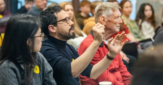A audience at a BRAID event. The camera is focused on one man who is talking and gesturing with his hands