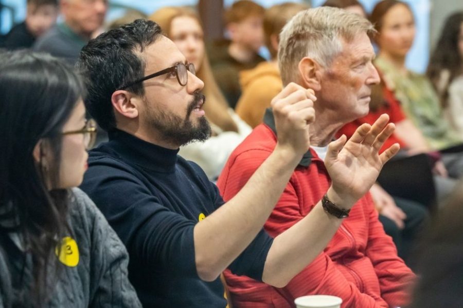 A audience at a BRAID event. The camera is focused on one man who is talking and gesturing with his hands